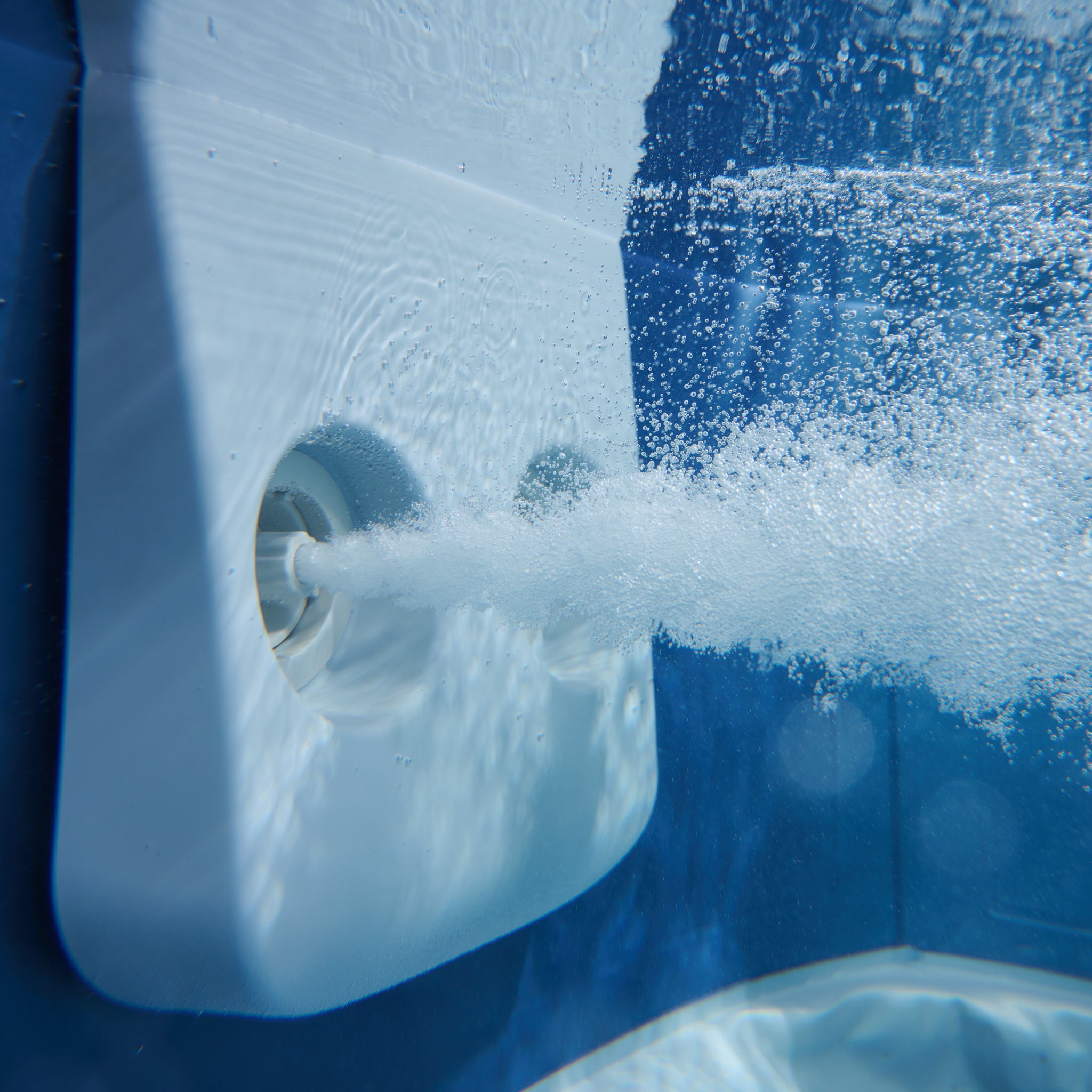 Underwater close up image of spa hydro jet blowing out a jet of bubbles into a portable hot tub jacuzzi with sapphire blue interior.